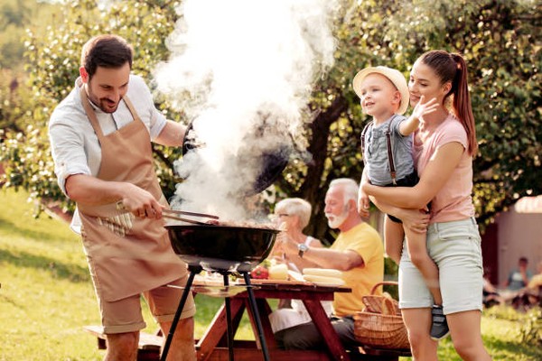 family grilling mother father baby and grandparents sitting in the backyard