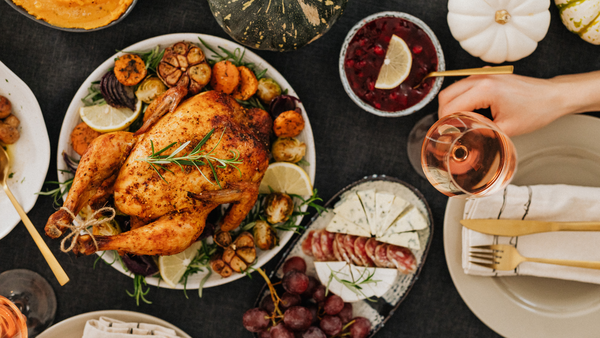 cooked turkey on a table with food and a hand holding a glass of wine