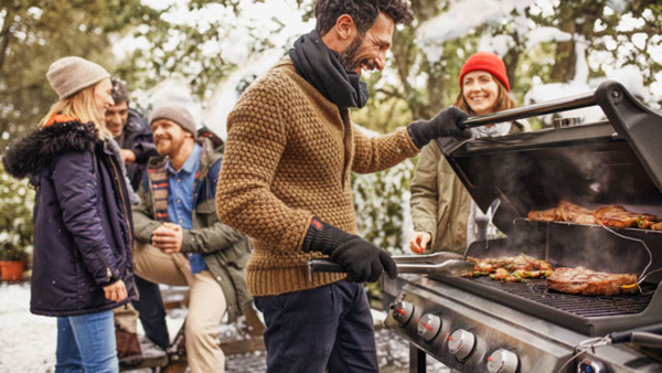 man doing barbecue at a grill with friends in the background