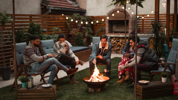 group of friends men and women roasting marshmallows at a firepit in the backyard